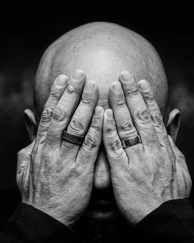 Retrato de alguém cobrindo o rosto com as mãos diante da câmera